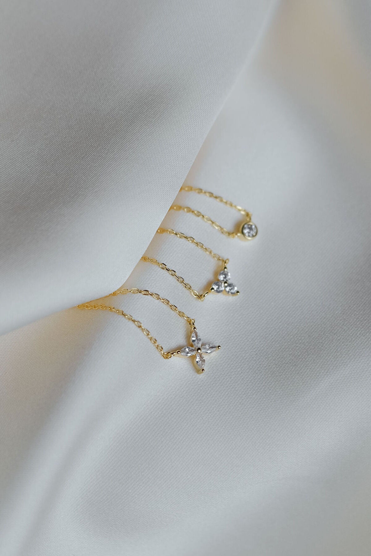 Three gold necklaces with gemstone pendants laid on a piece of silk