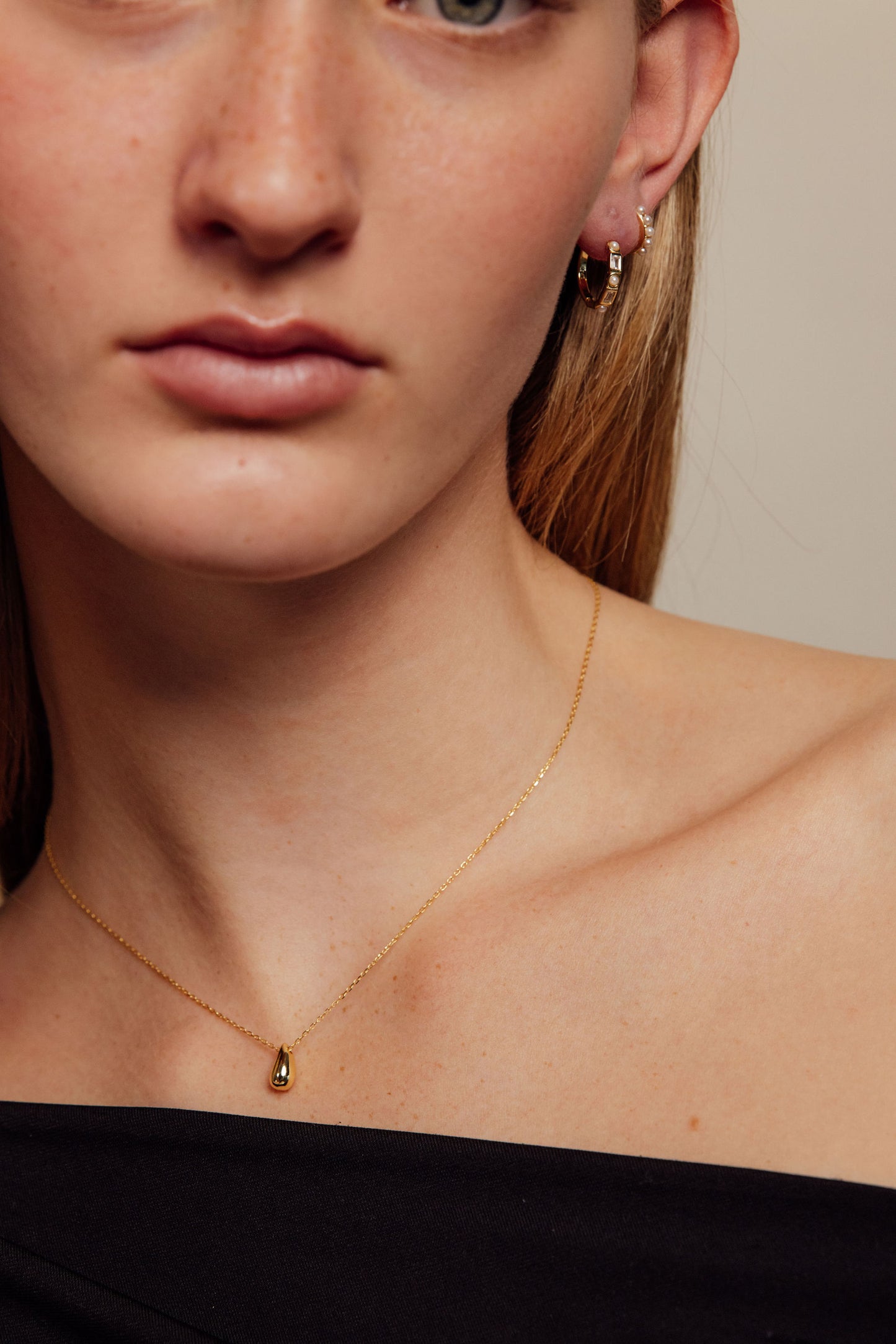 Close-up of a person wearing a gold necklace and gold earrings against a neutral background