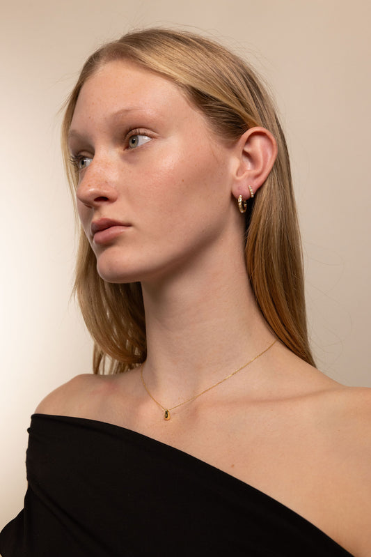 Woman wearing gold earrings and a gold necklace against a plain background