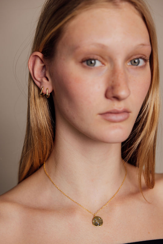 Woman wearing a gold necklace and earrings against a neutral background