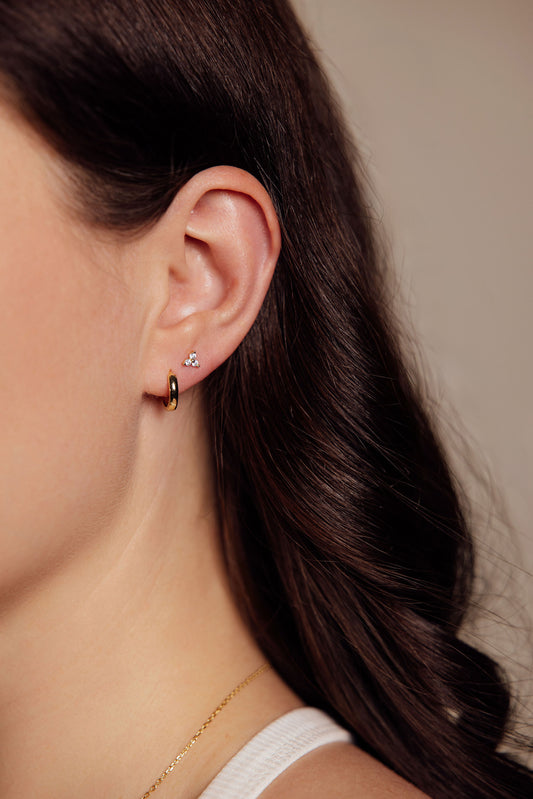 Close-up of a woman wearing gold earrings with a neutral background