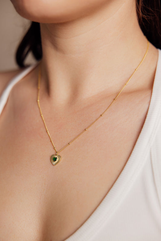 Gold necklace with a green heart pendant worn by a person in a white top.