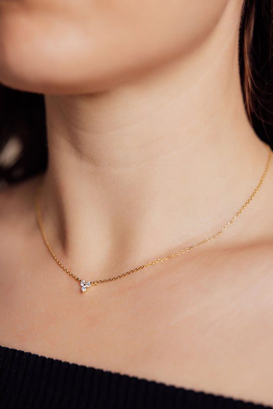 Gold necklace with a pendant featuring three gemstones on a person wearing a black top.