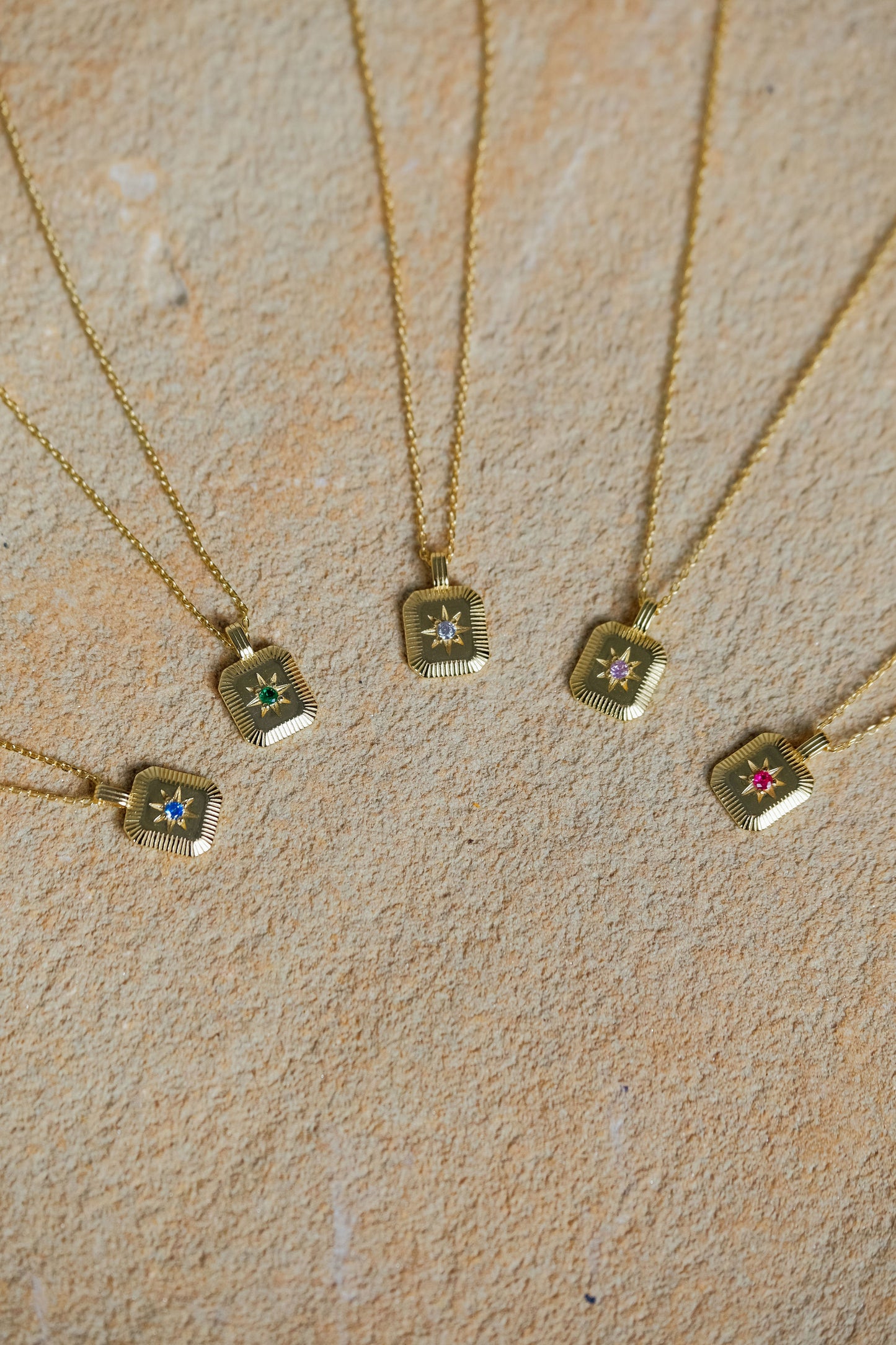 Gold necklaces with small square pendants on a beige surface