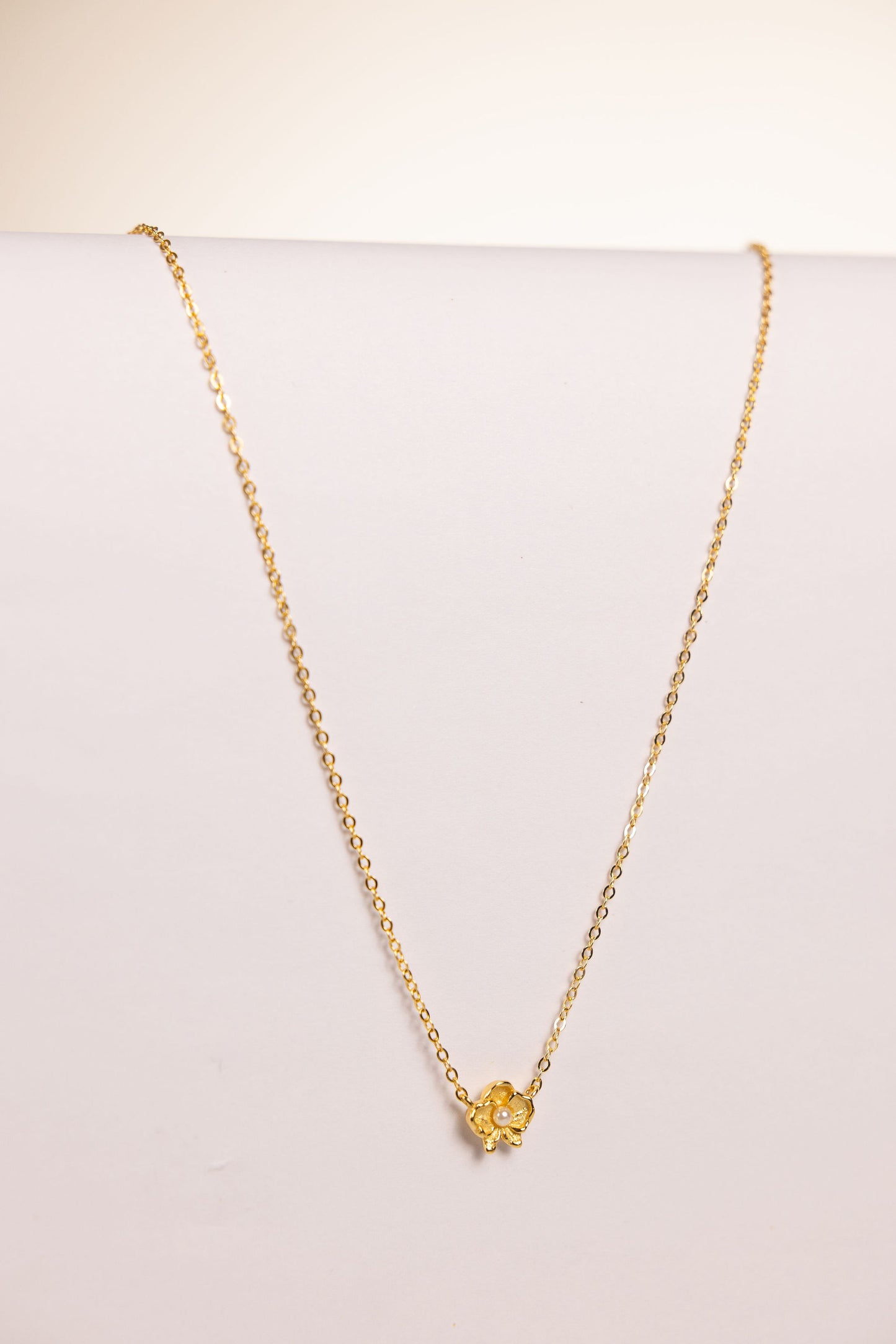 Gold necklace with a floral pendant featuring a pearl on a white background