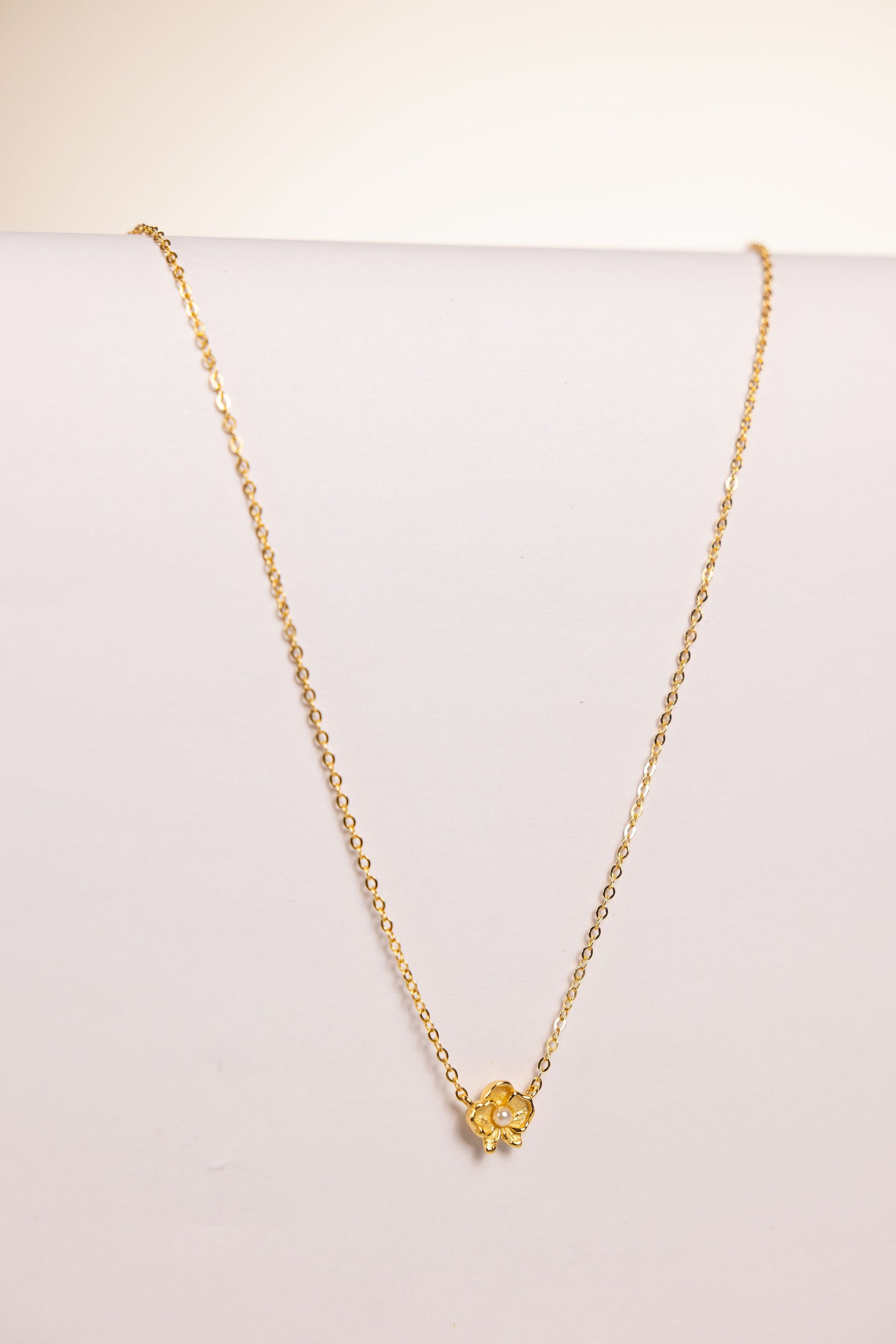 Gold necklace with a floral pendant featuring a pearl on a white background