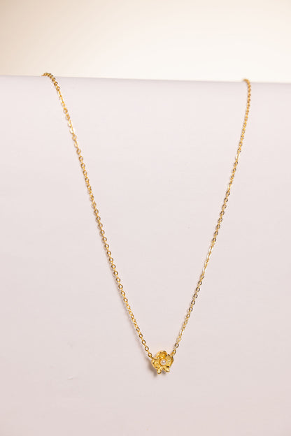Gold necklace with a floral pendant featuring a pearl on a white background