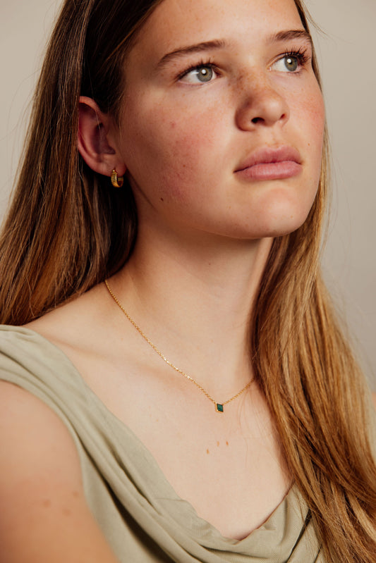 Close-up of a woman wearing a gold necklace with a green pendant against a neutral background