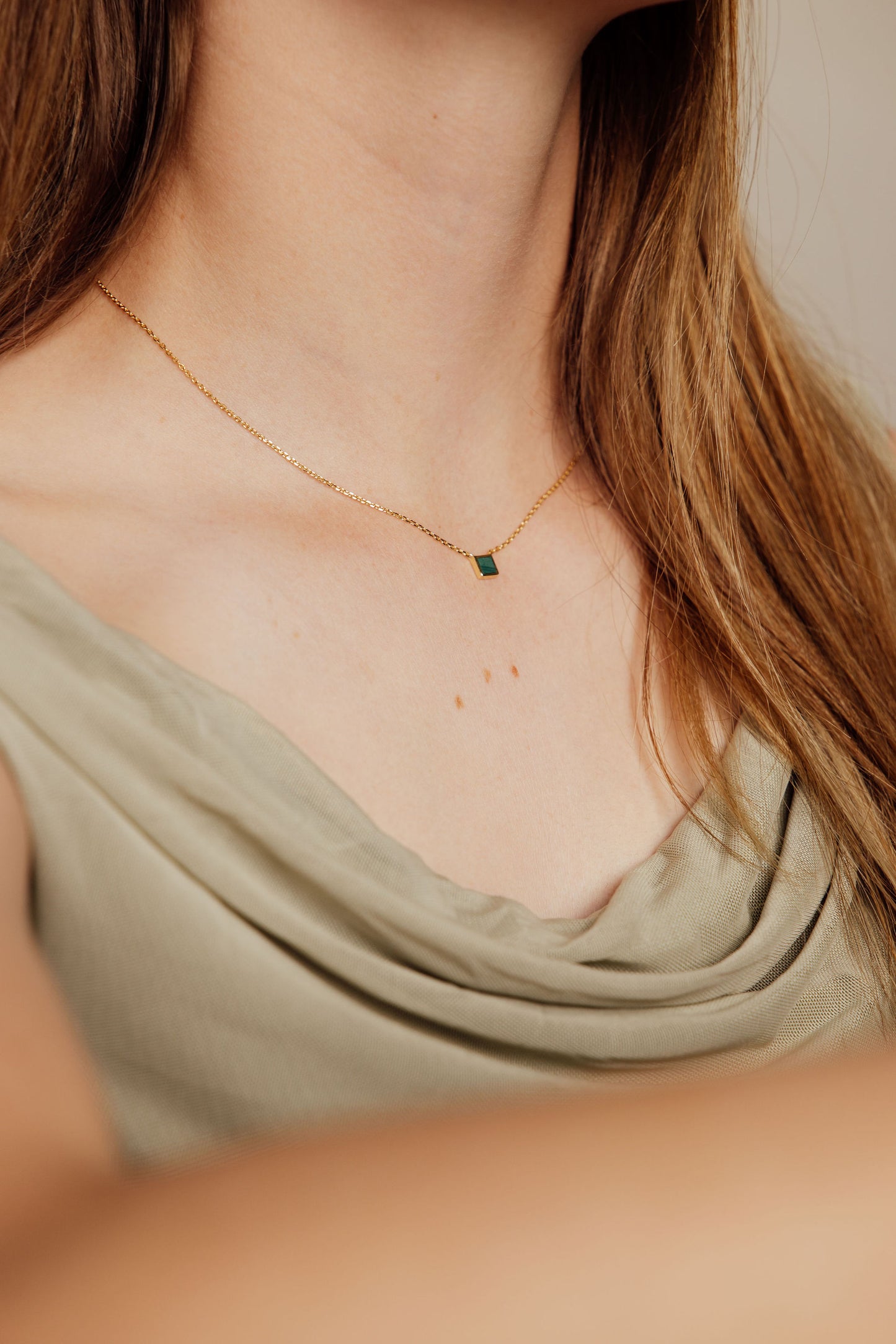 Close-up of a person wearing a gold necklace with a green malachite gemstone.