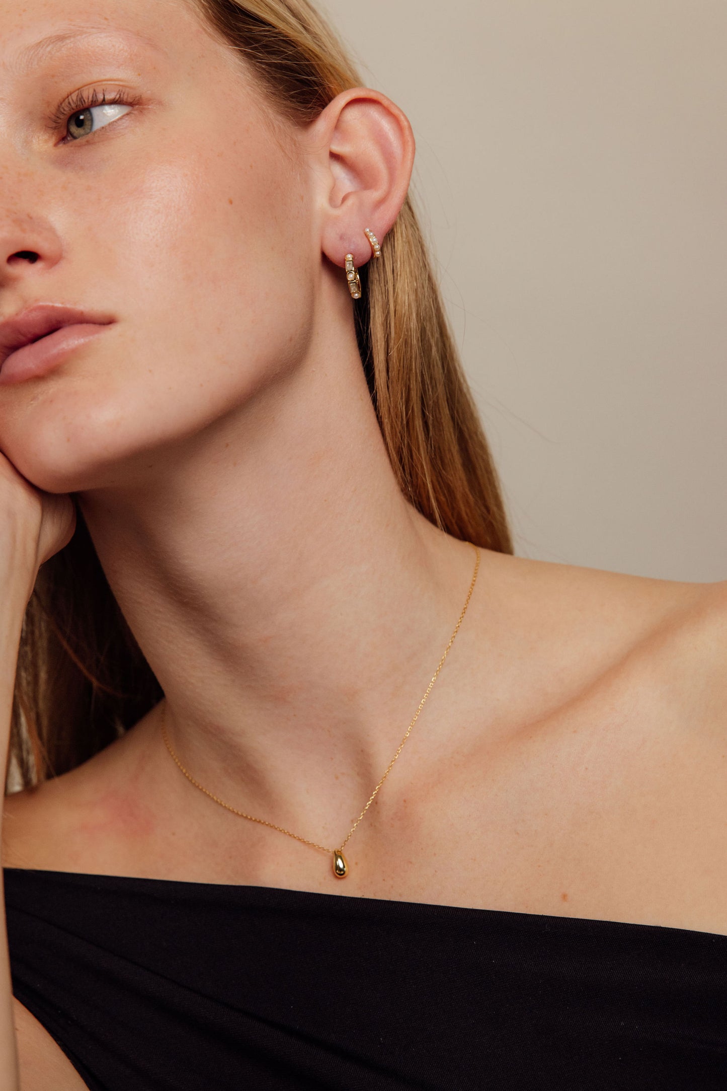 Close-up of a person wearing gold earrings and a necklace against a neutral background