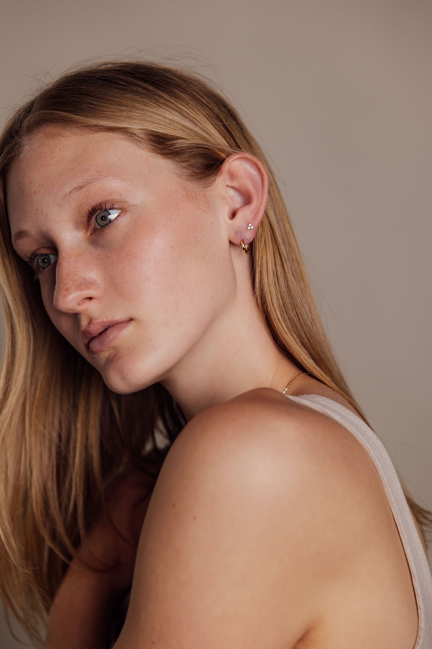 Woman with blonde hair wearing gold earrings against a neutral background