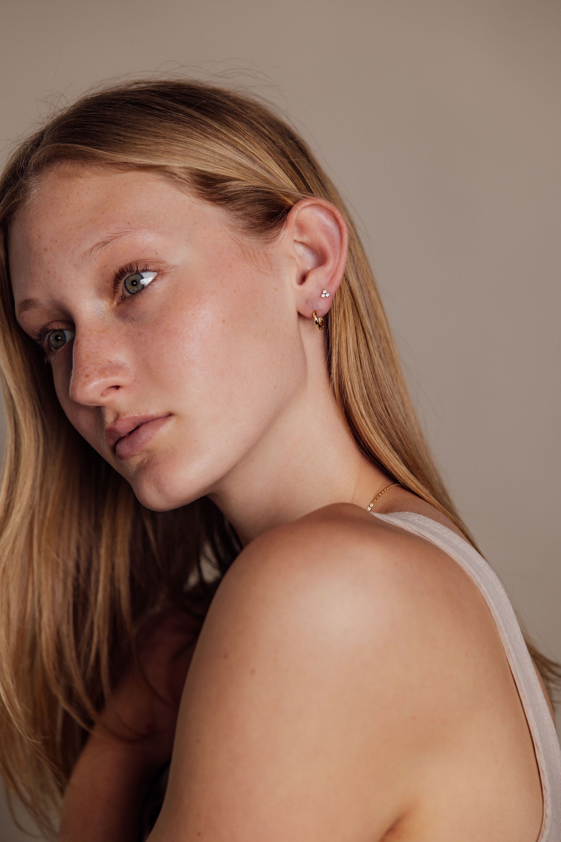 Woman with blonde hair wearing gold earrings against a neutral background