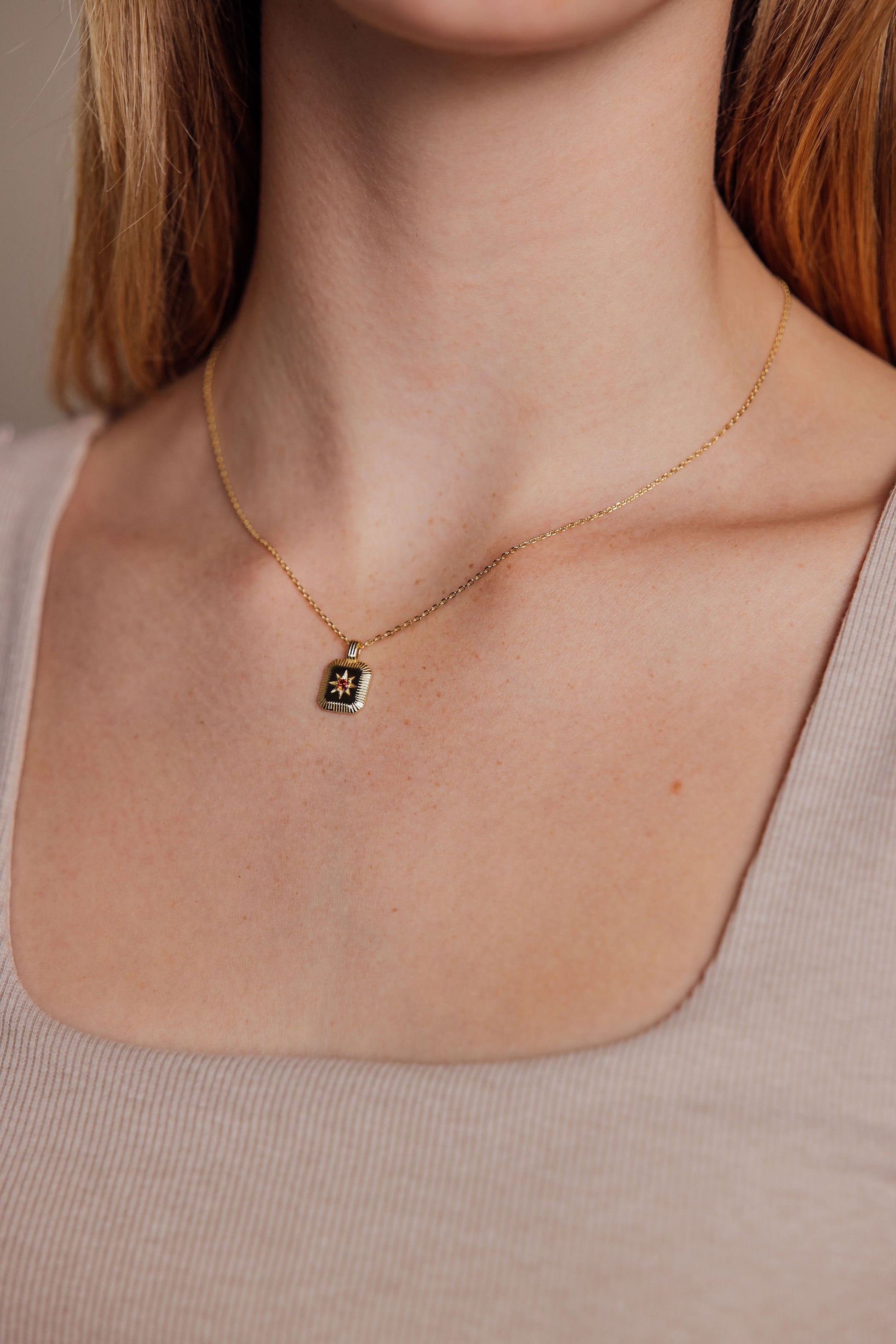 Gold necklace with a small pendant on a person wearing a beige top.