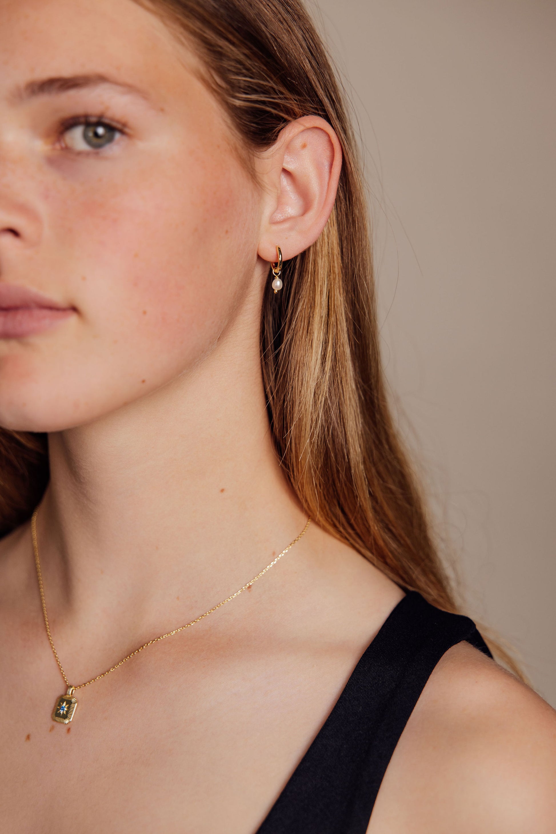 Close-up of a woman wearing gold earrings and gold necklace against a neutral background