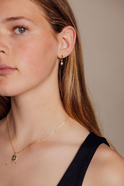 Close-up of a woman wearing gold earrings and gold necklace against a neutral background