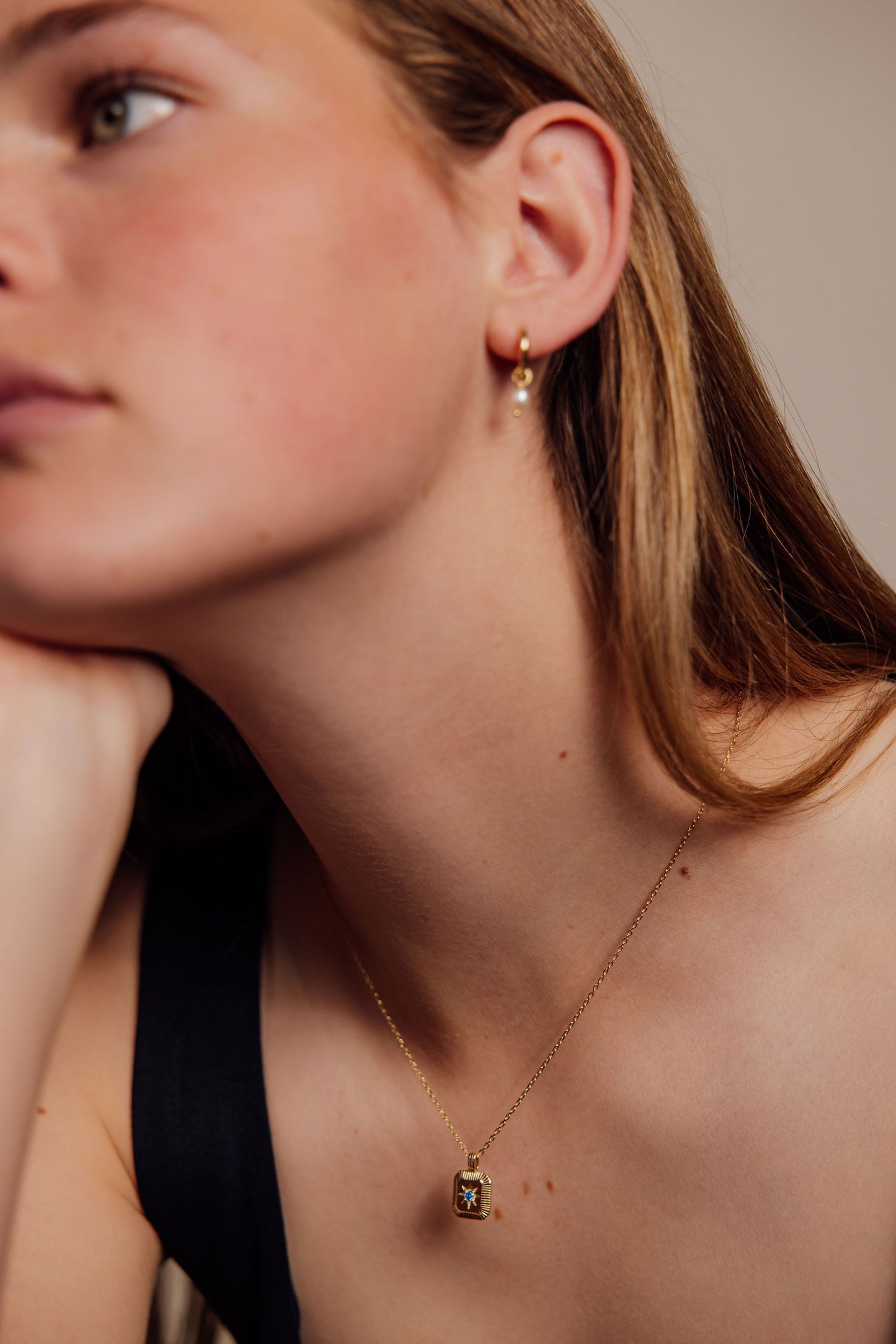 Close-up of a person wearing gold earrings and a necklace against a neutral background