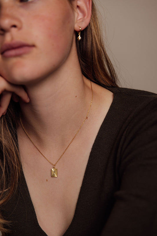 Close-up of a person wearing gold jewelry including earrings and a necklace.