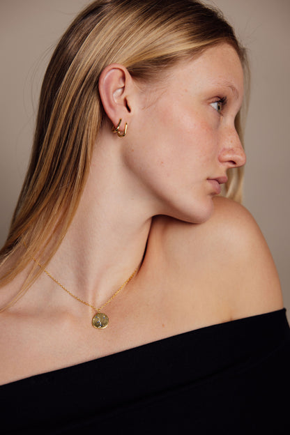 Woman wearing a gold earrings and necklace against a neutral background