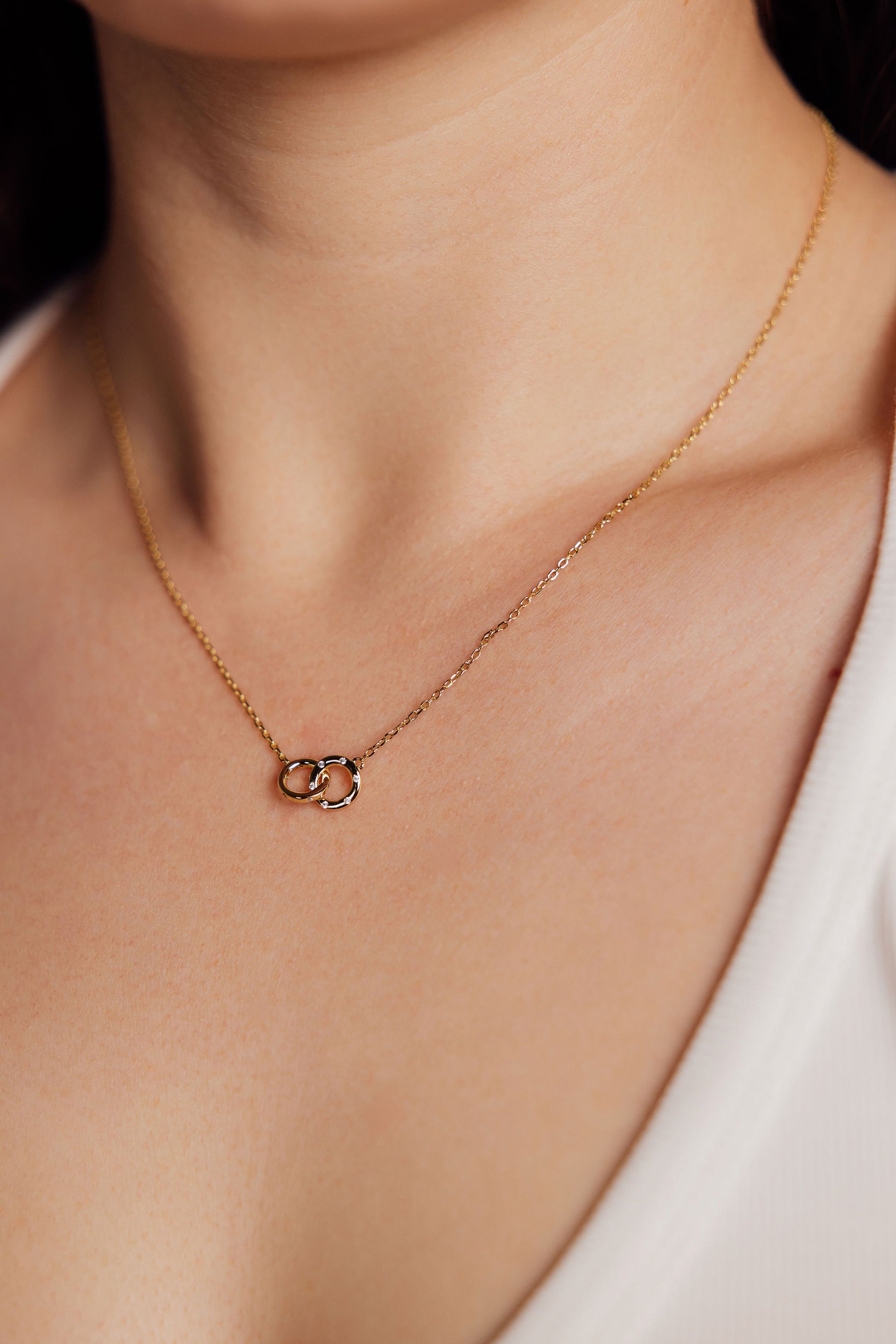 Close up of gold necklace with a small pendant on a person wearing a white top.