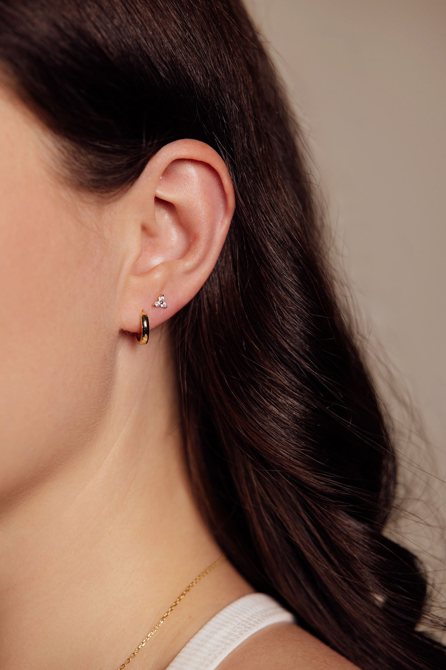 Close-up of a woman wearing gold earrings with a neutral background