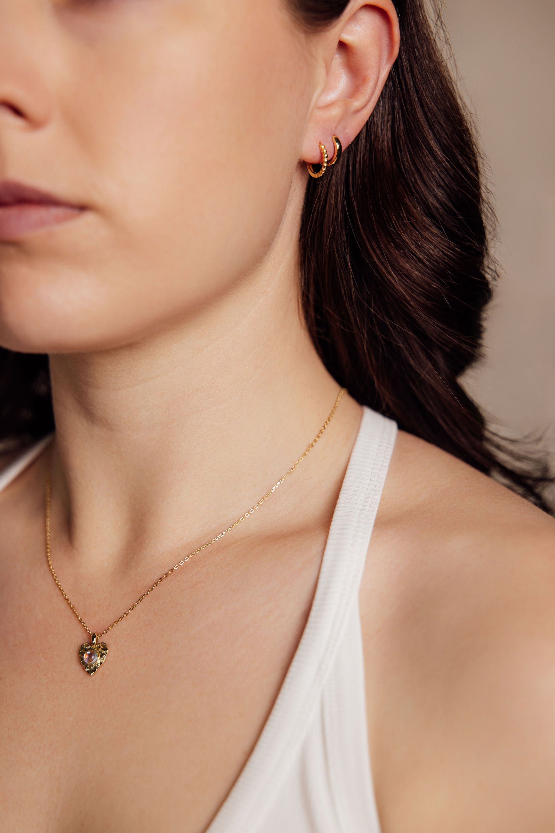 Close-up of a woman wearing gold earrings and a gold necklace with a heart pendant