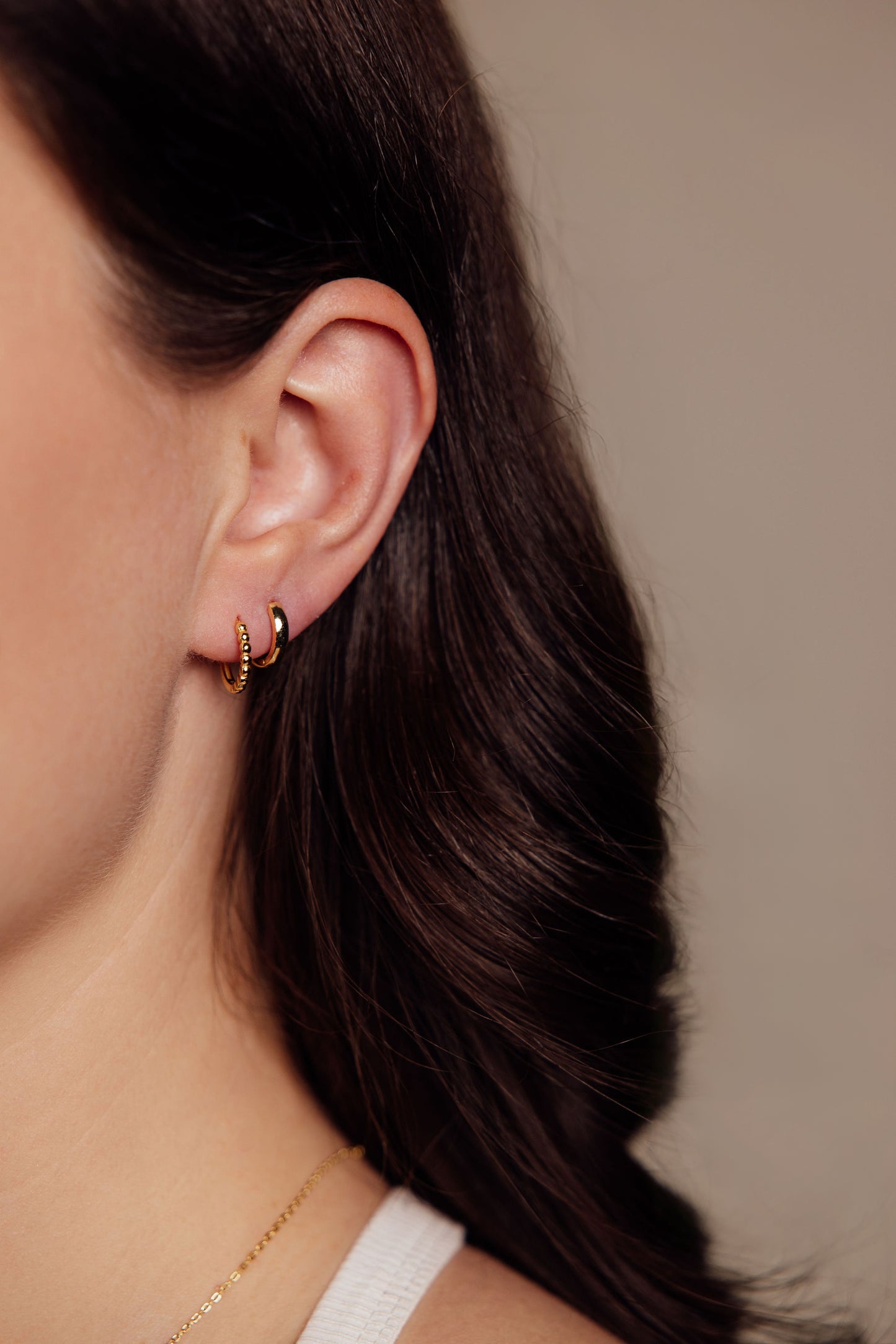 Close-up of a woman wearing gold hoop earrings with a neutral background