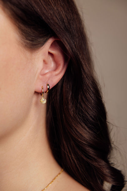 Close-up of a person wearing gold earrings with a neutral background