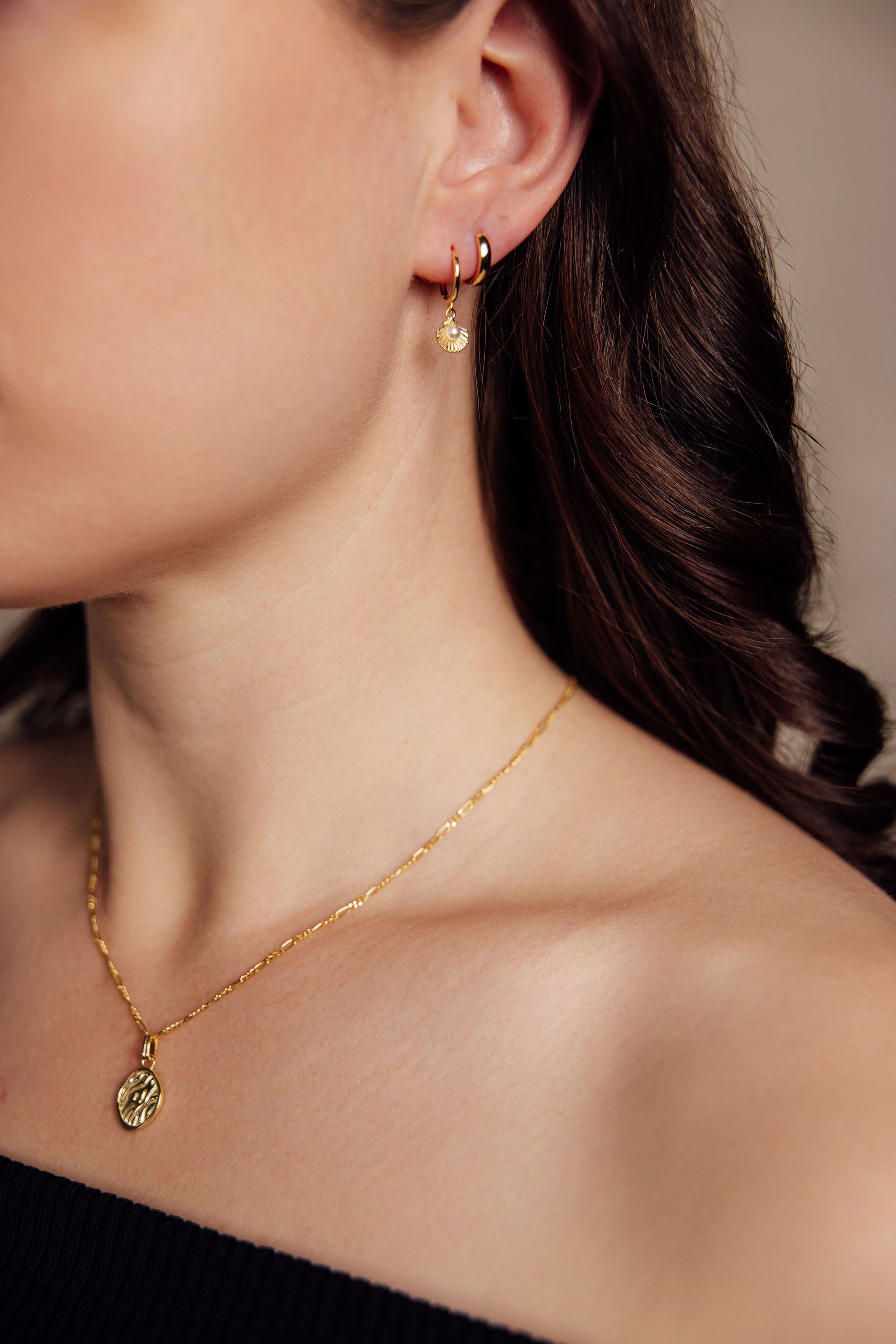 Close-up of a person wearing gold earrings and a gold necklace against a neutral background