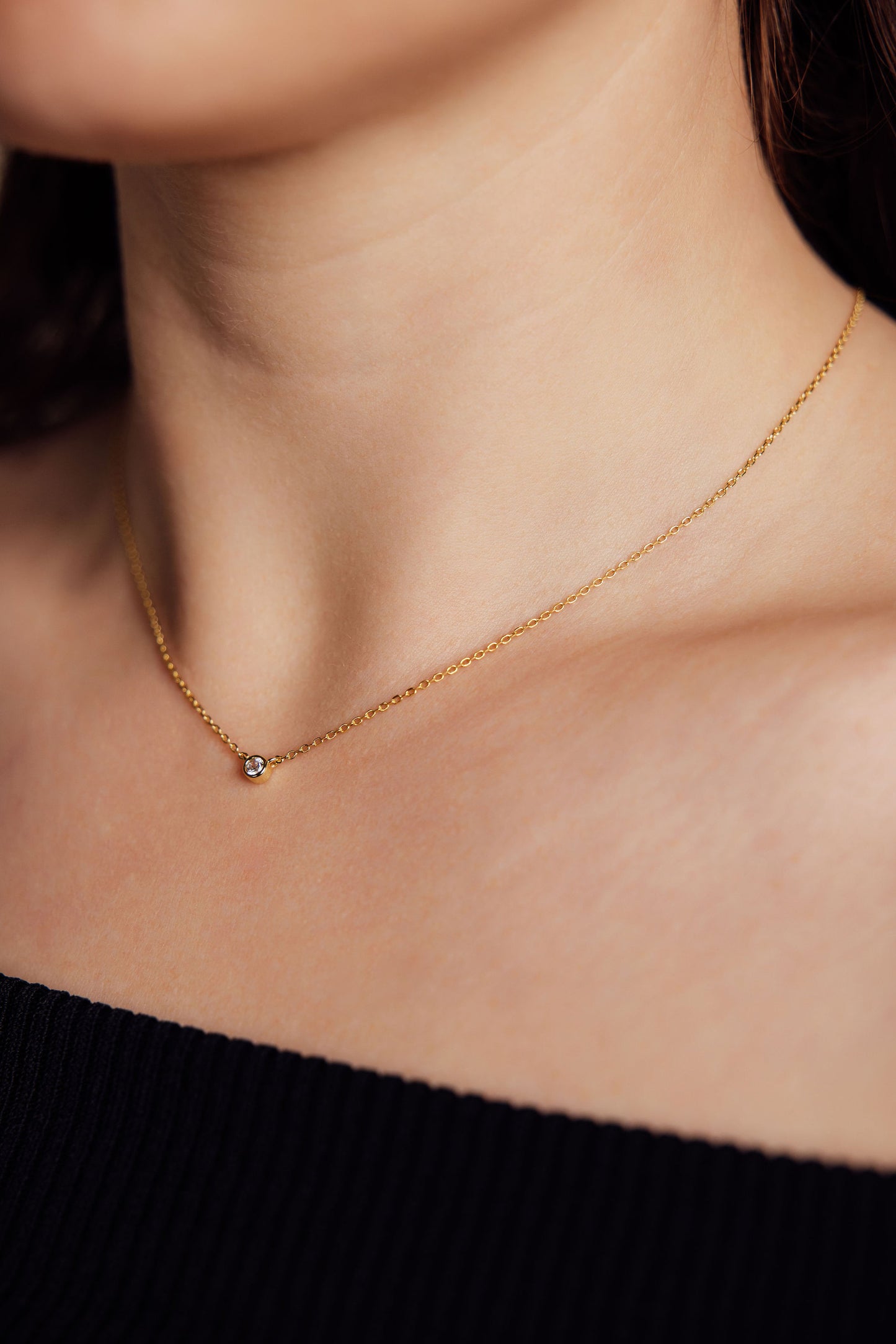 Gold necklace with a small gemstone pendant on a person wearing a black top.