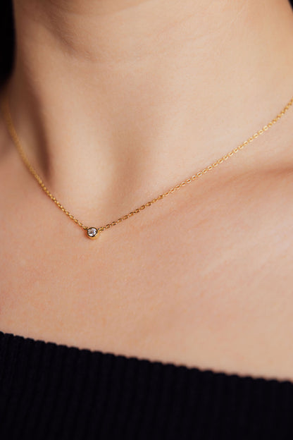 Gold necklace with a small round gemstone pendant on a person