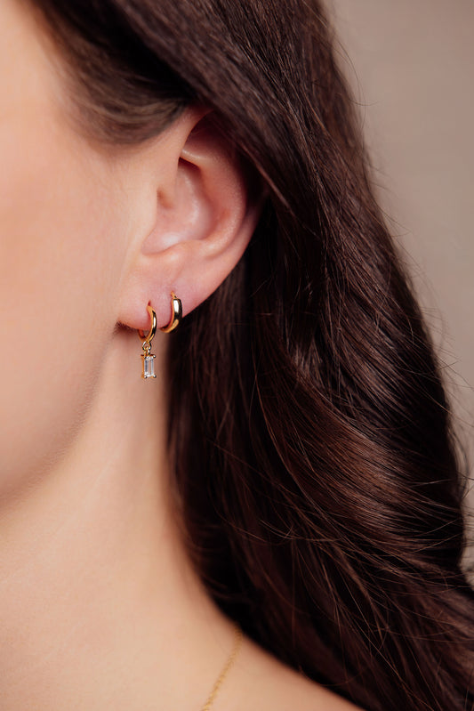 Close-up of a person wearing gold earrings with a neutral background