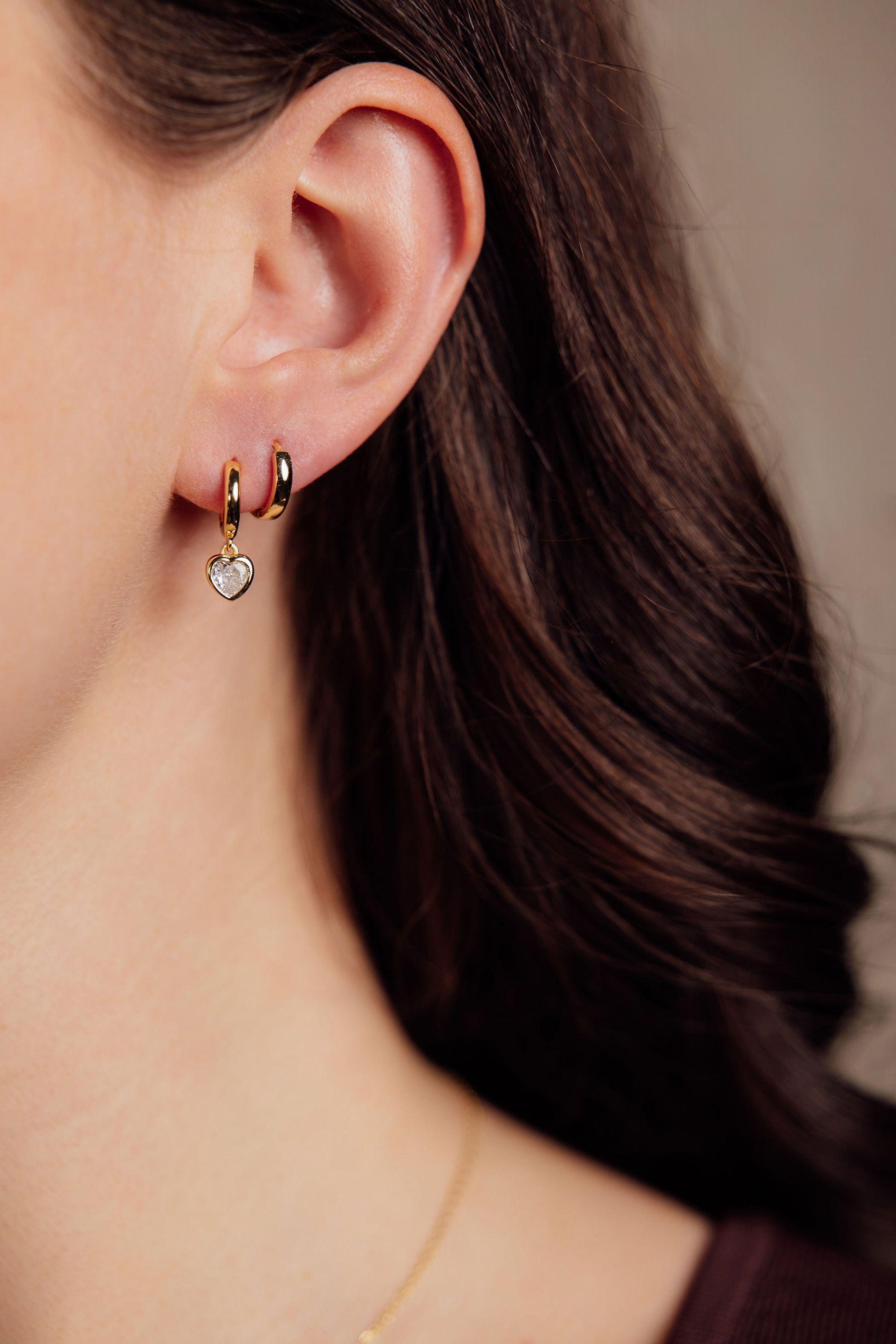 Close-up of a person wearing gold hoop earrings with heart charms.