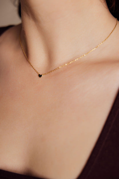 Gold necklace with a small heart pendant on a woman's neck against a neutral background