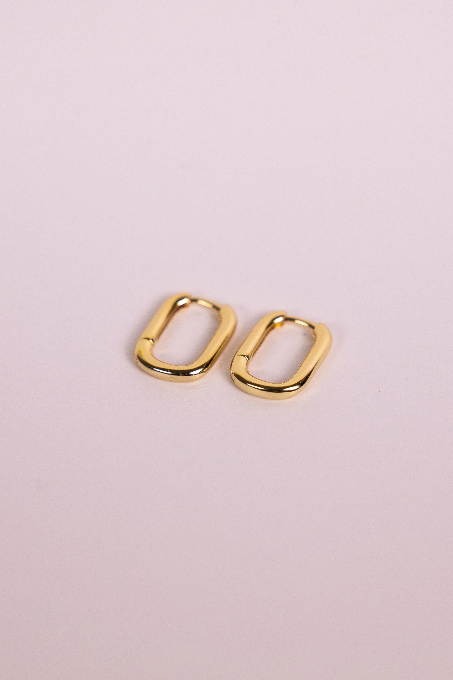 Gold oblong hoop earrings on a neutral background