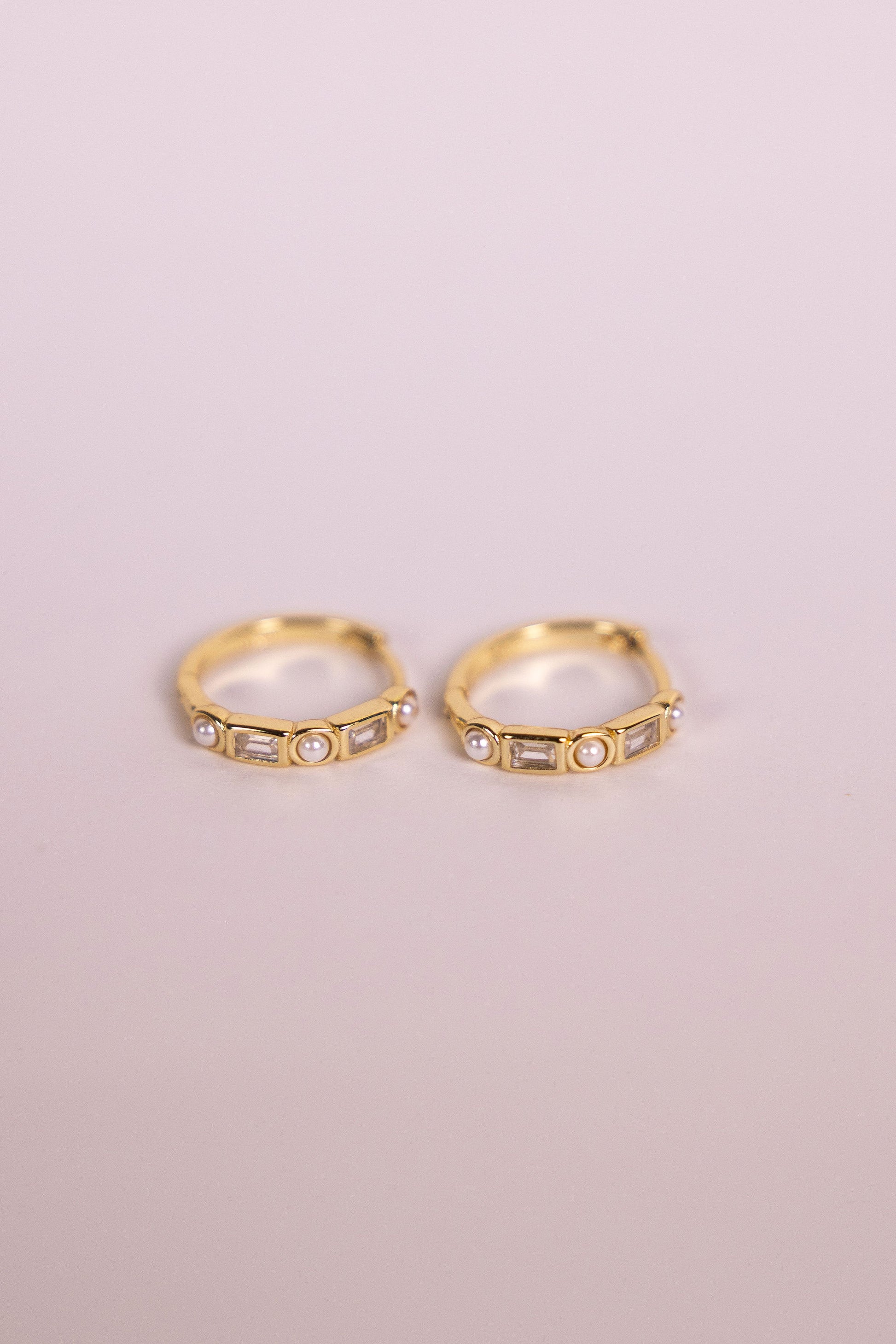 Gold earrings featuring gemstones and pearls on a neutral background