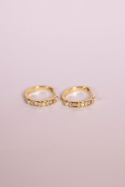 Gold earrings featuring gemstones and pearls on a neutral background
