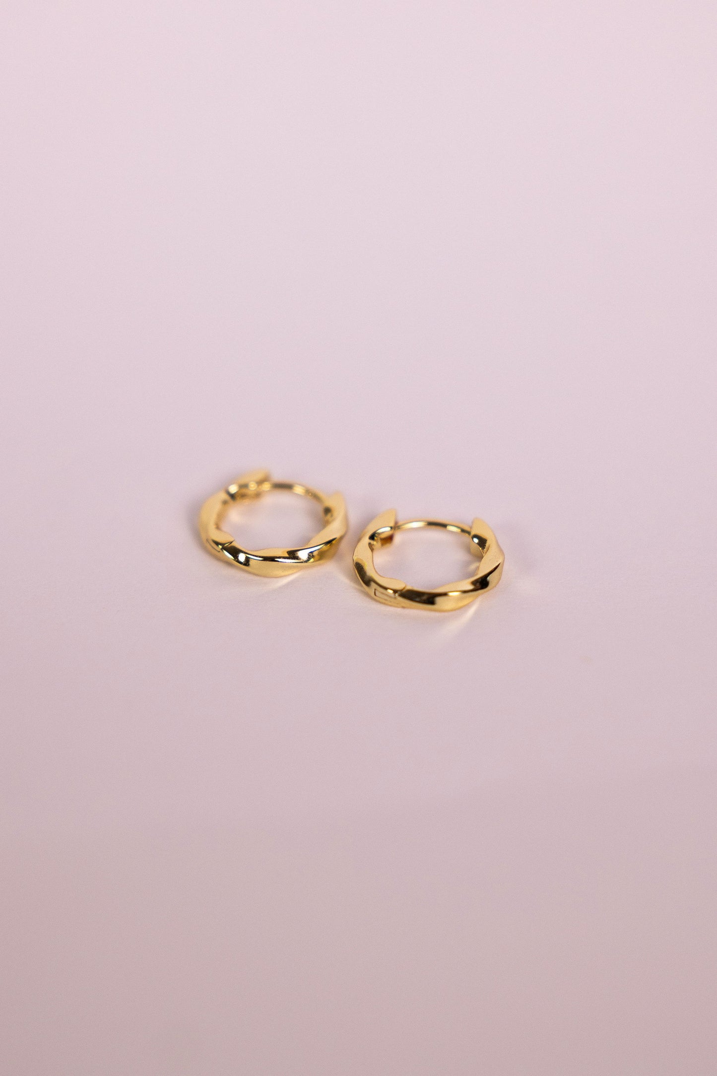 Gold twisted hoop earrings on a neutral background