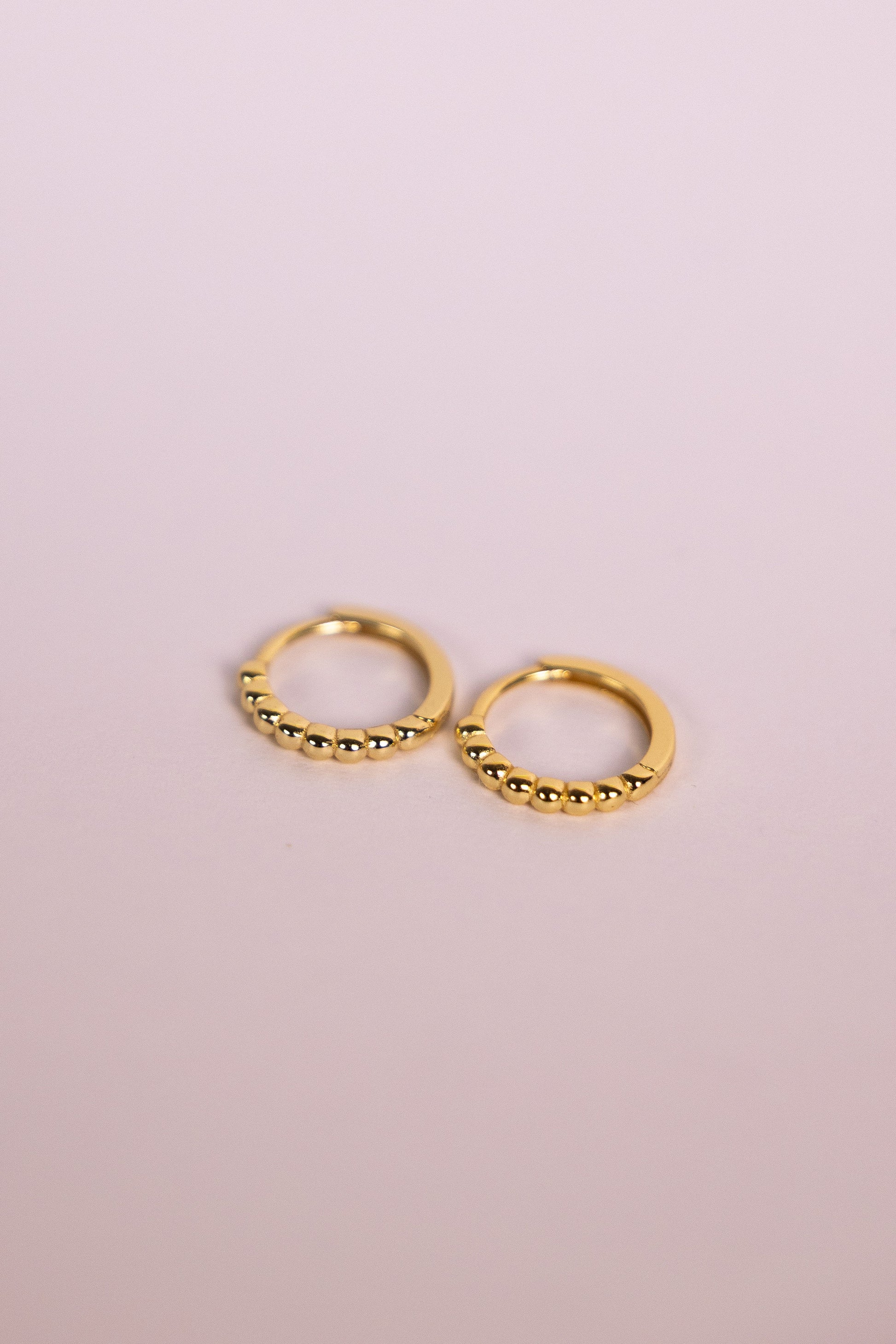 Gold bead hoop earrings on a neutral background