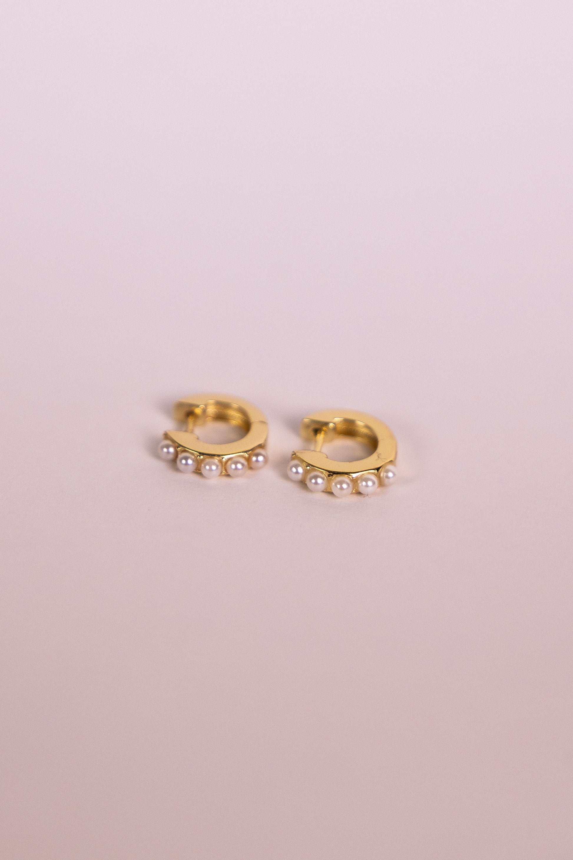 Gold hoop earrings with pearl accents on a neutral background