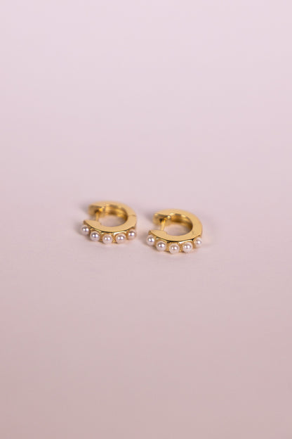 Gold hoop earrings with pearl accents on a neutral background