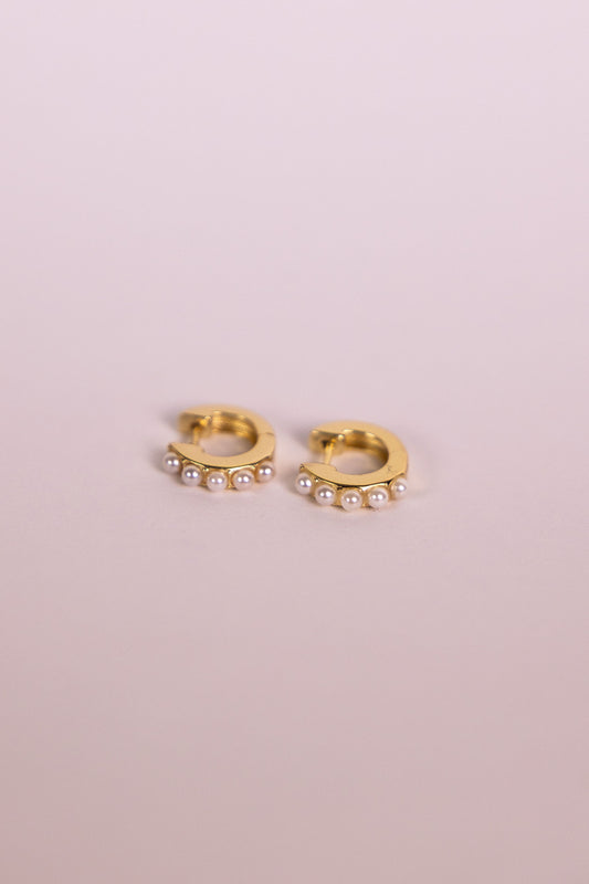 Gold hoop earrings with pearl accents on a neutral background