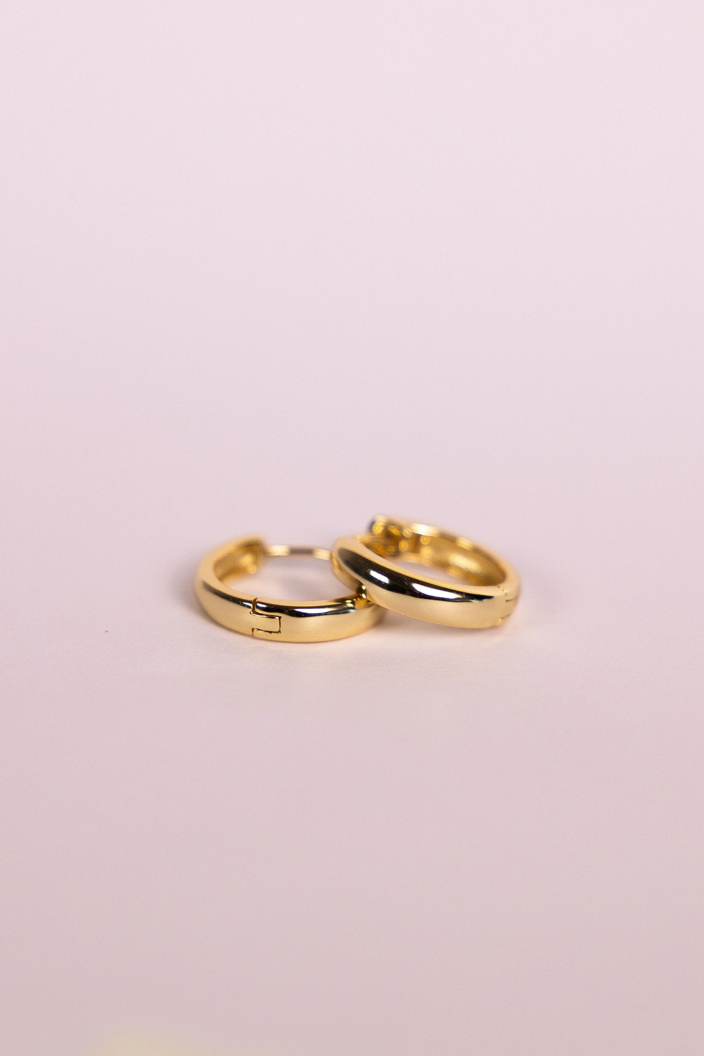 Two gold hoop earrings on a neutral background