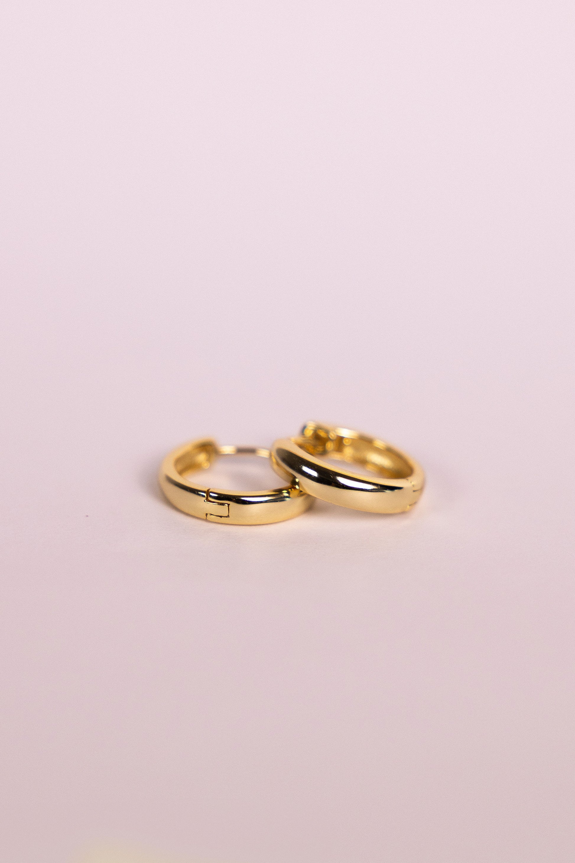 Two gold hoop earrings on a neutral background