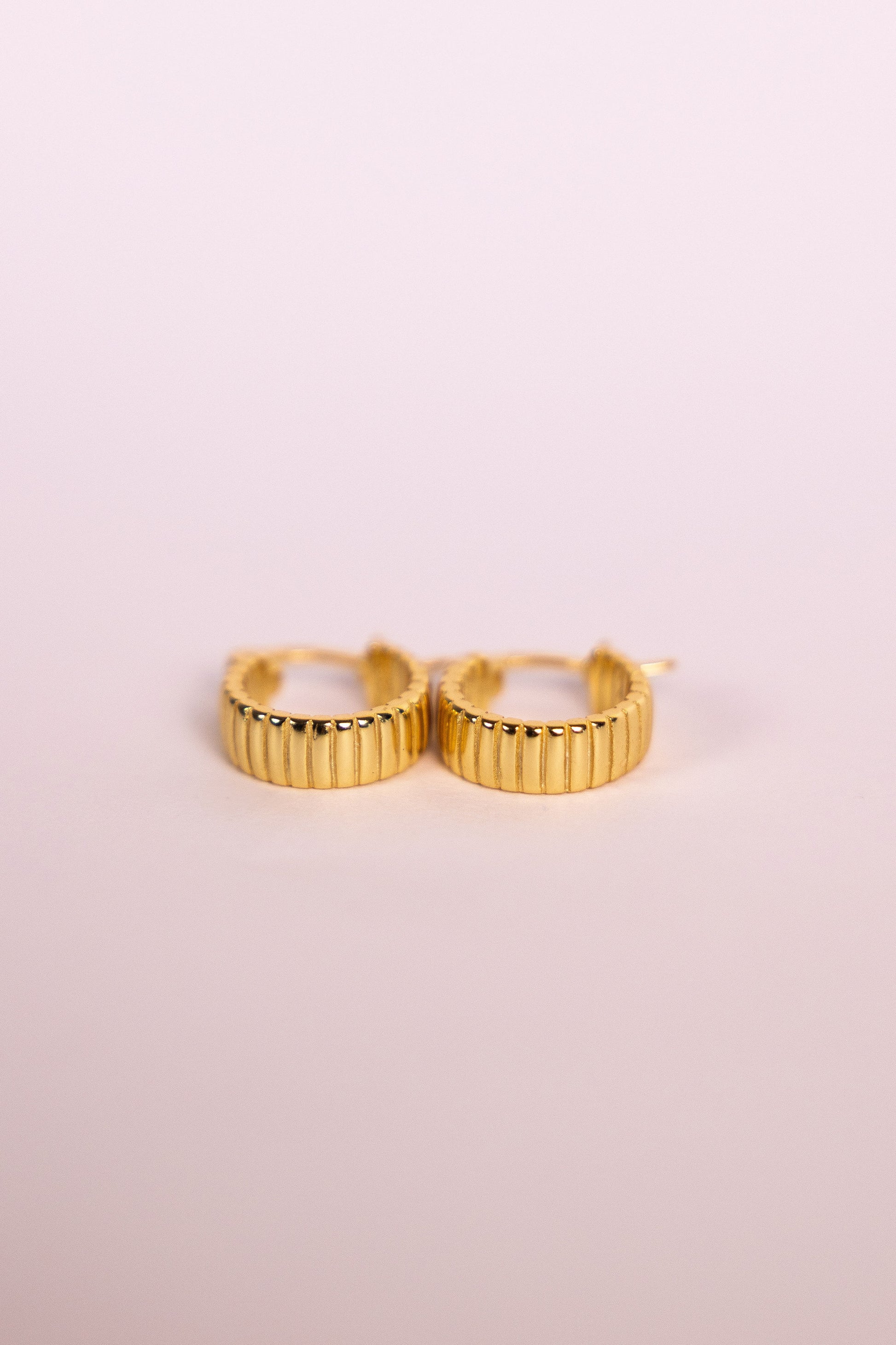Gold hoop earrings on a light pink background
