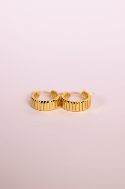 Gold hoop earrings on a light pink background