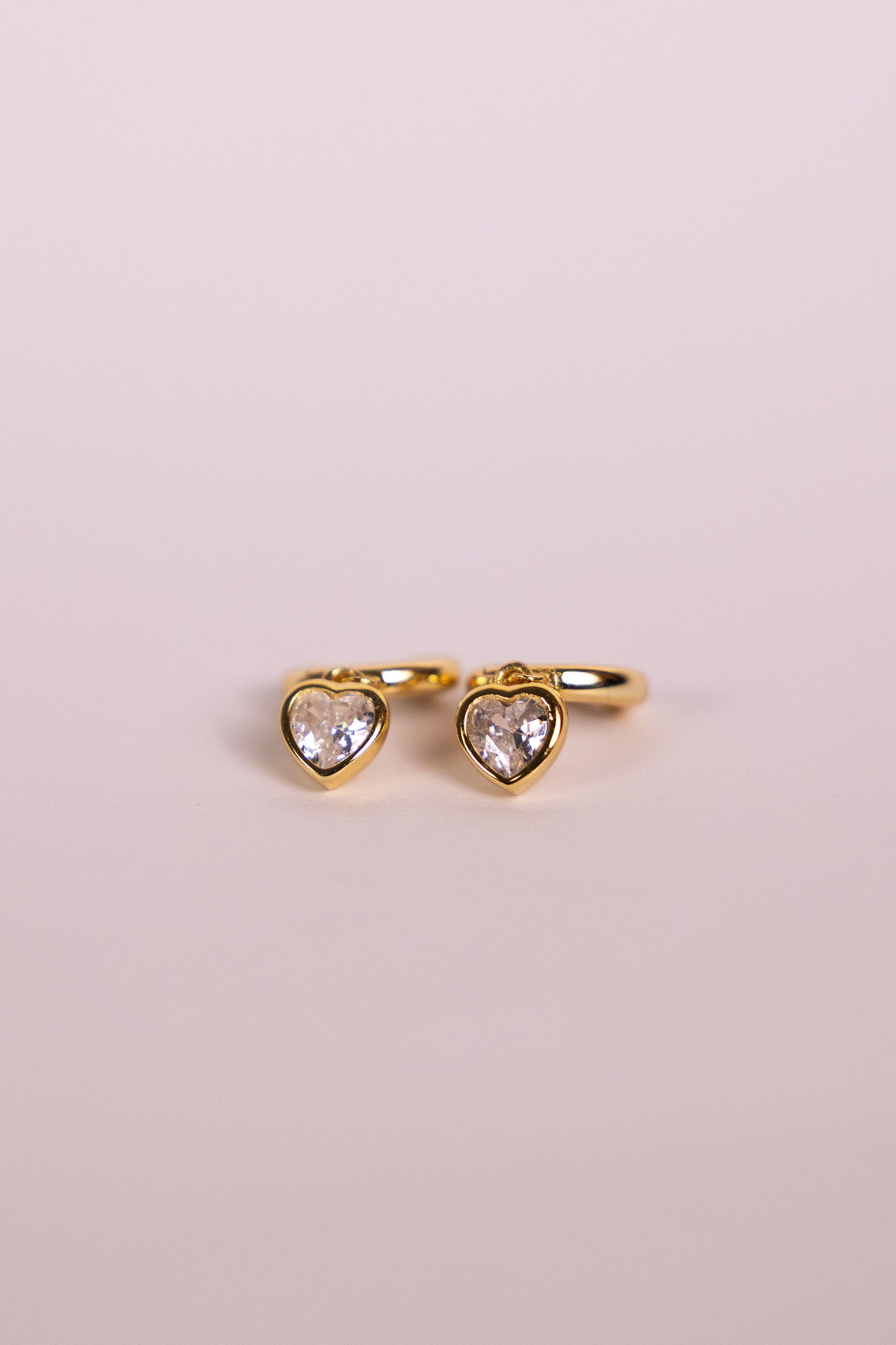 Gold earrings with a heart-shaped charm on a neutral background
