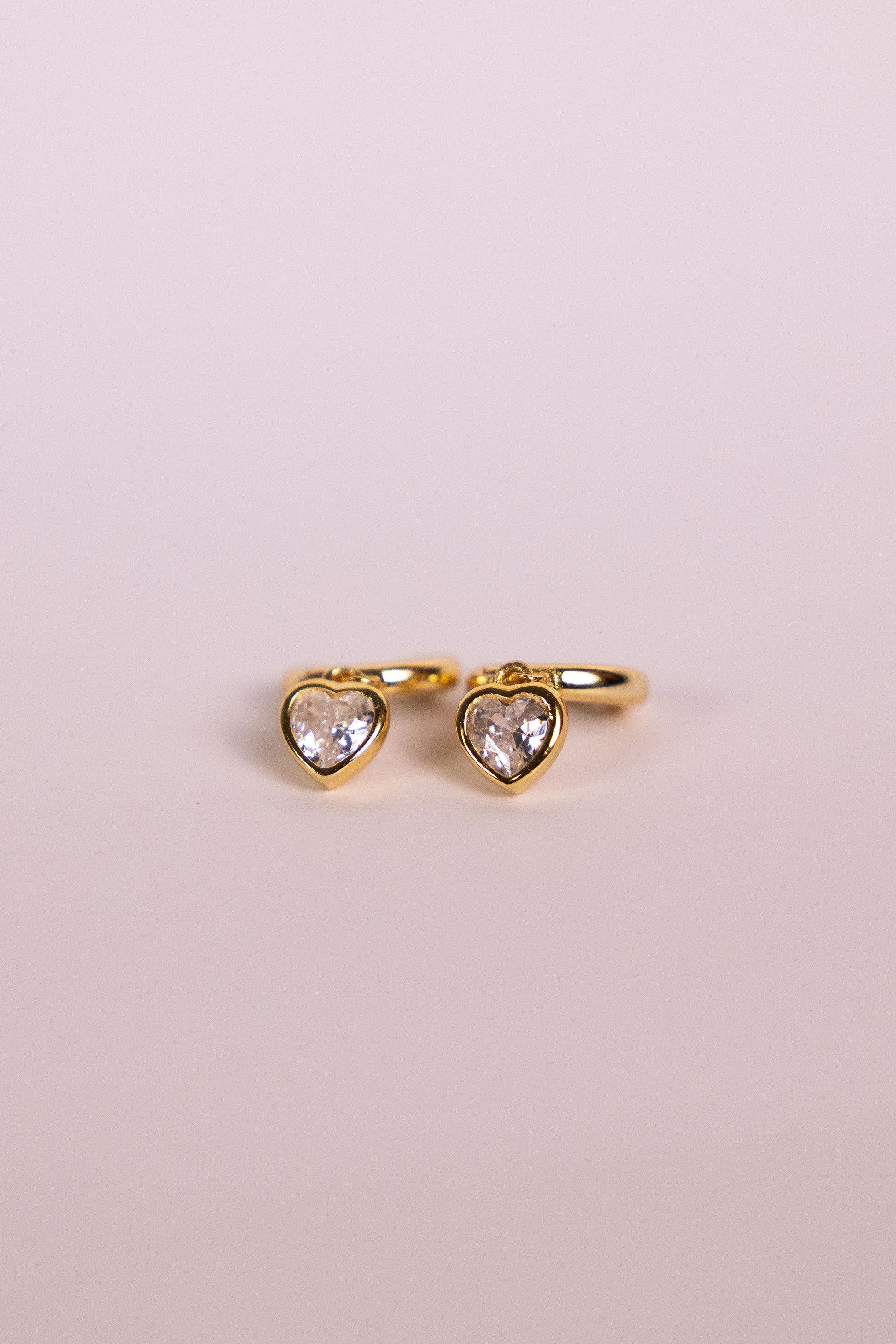 Gold earrings with a heart-shaped charm on a neutral background