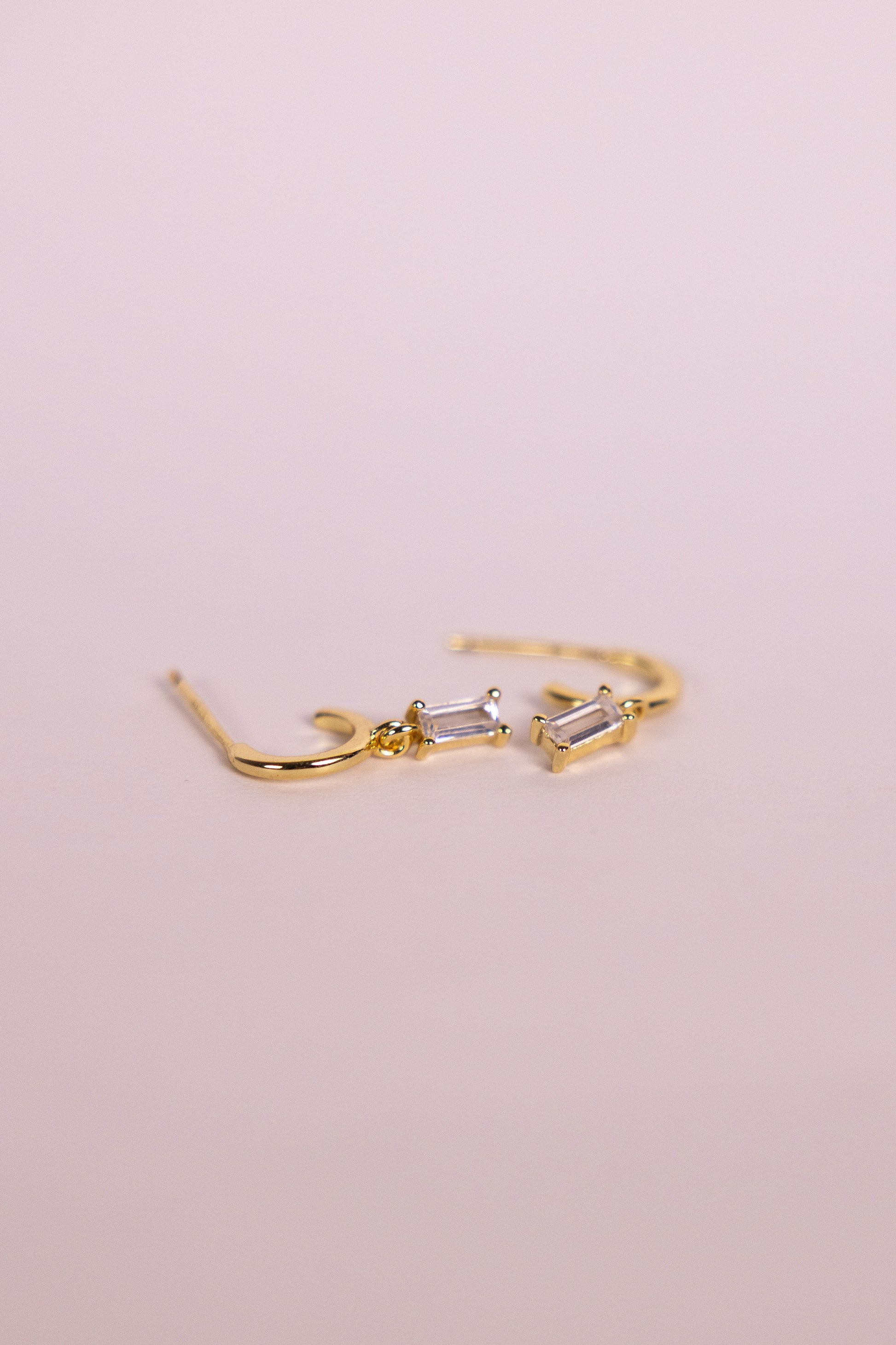 Gold earrings with a rectangular gemstone charm on a neutral background
