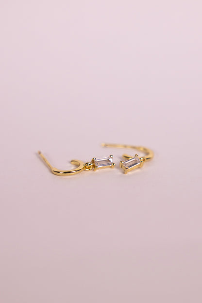 Gold earrings with a rectangular gemstone charm on a neutral background
