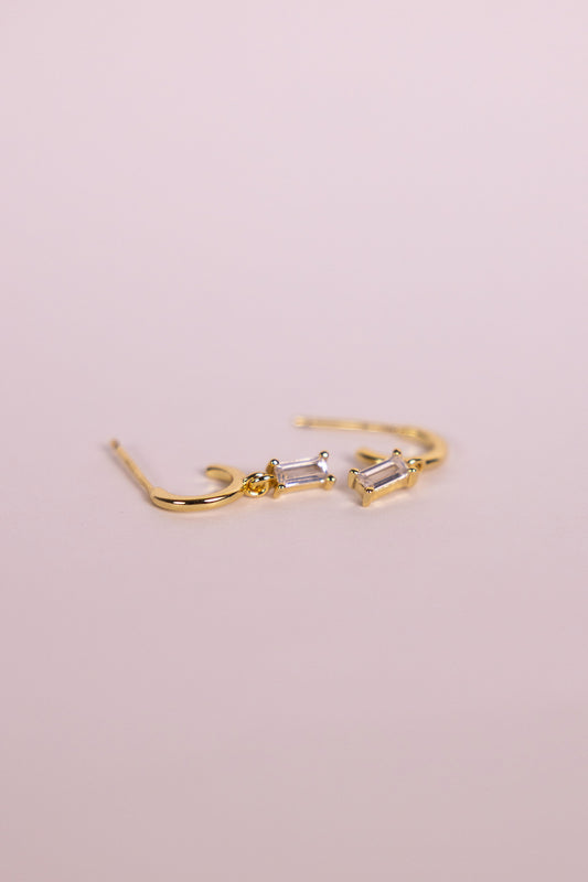 Gold earrings with a rectangular gemstone charm on a neutral background